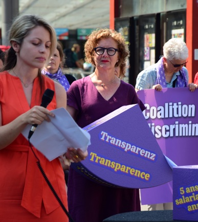 Mehrere Personen mit lila Schildern kämpfen für Gleichstellung beim Lohn und stehen am Bern Bahnhof